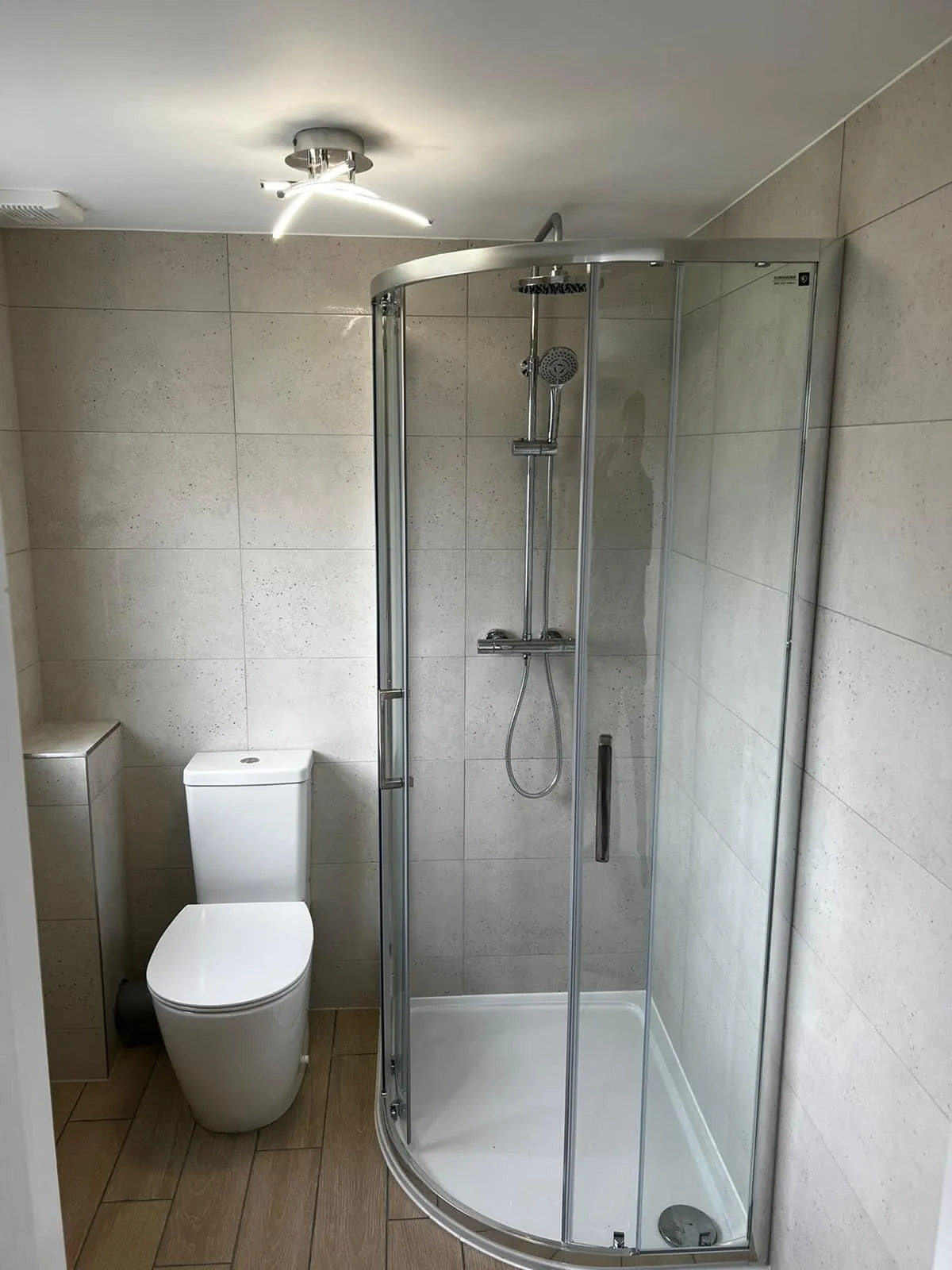 Modern bathroom featuring a glass shower enclosure, white toilet, and neutral tiled walls with a sleek ceiling light.