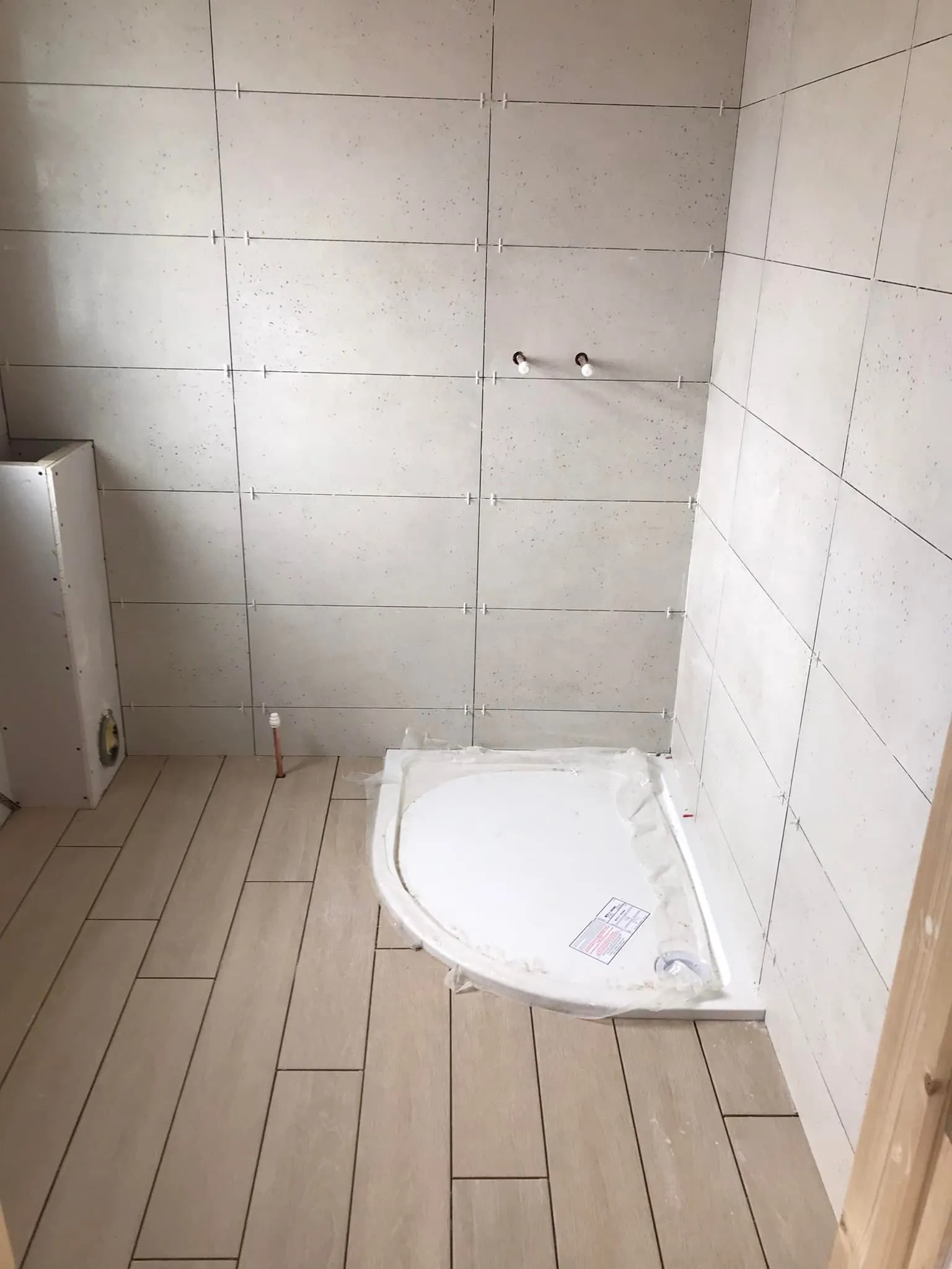 A partially completed bathroom featuring light-colored tiled walls and floor, with a shower base installed in the corner.