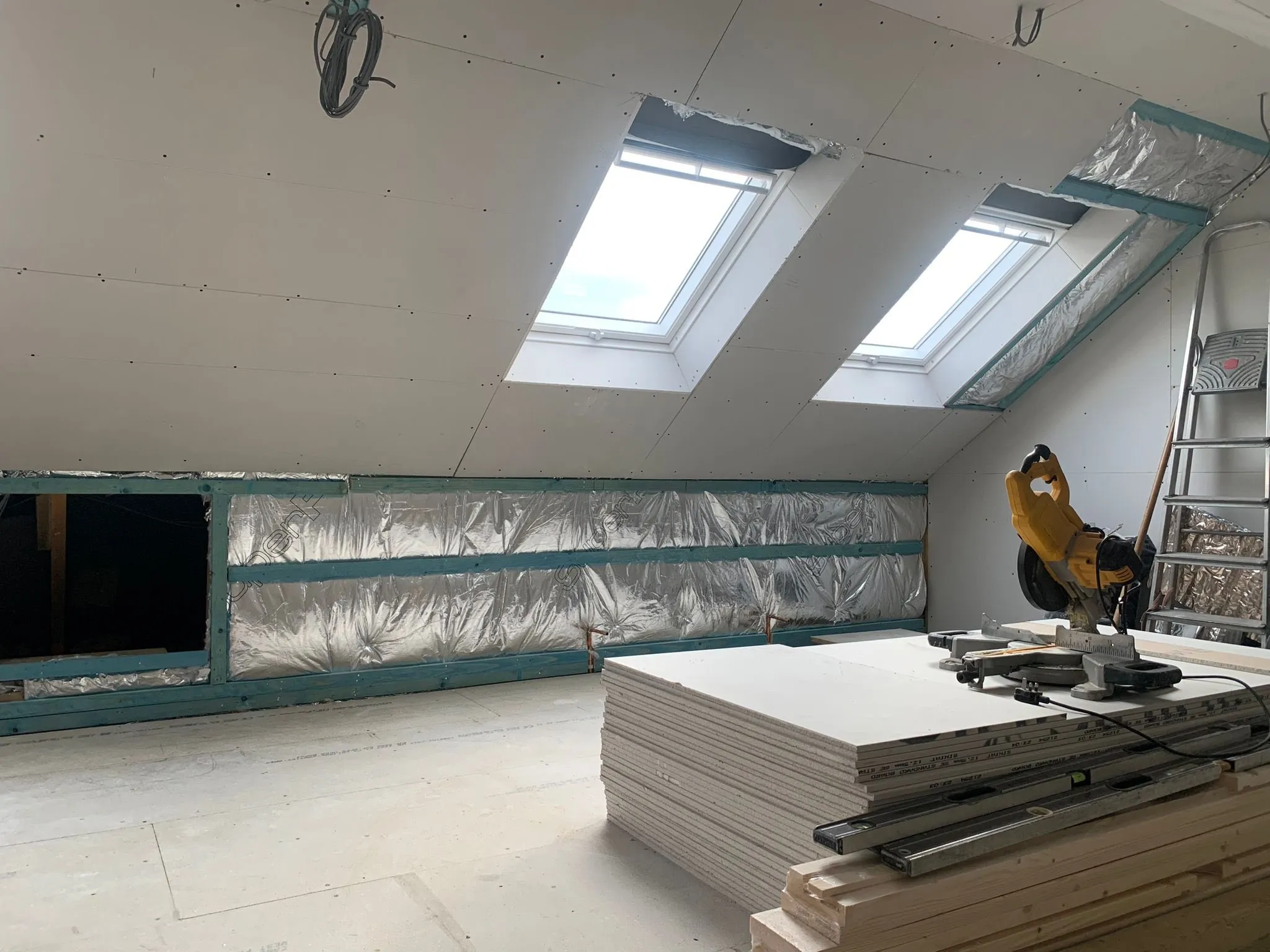 Interior of a renovated attic with skylights, drywall installation ongoing, and construction tools visible.