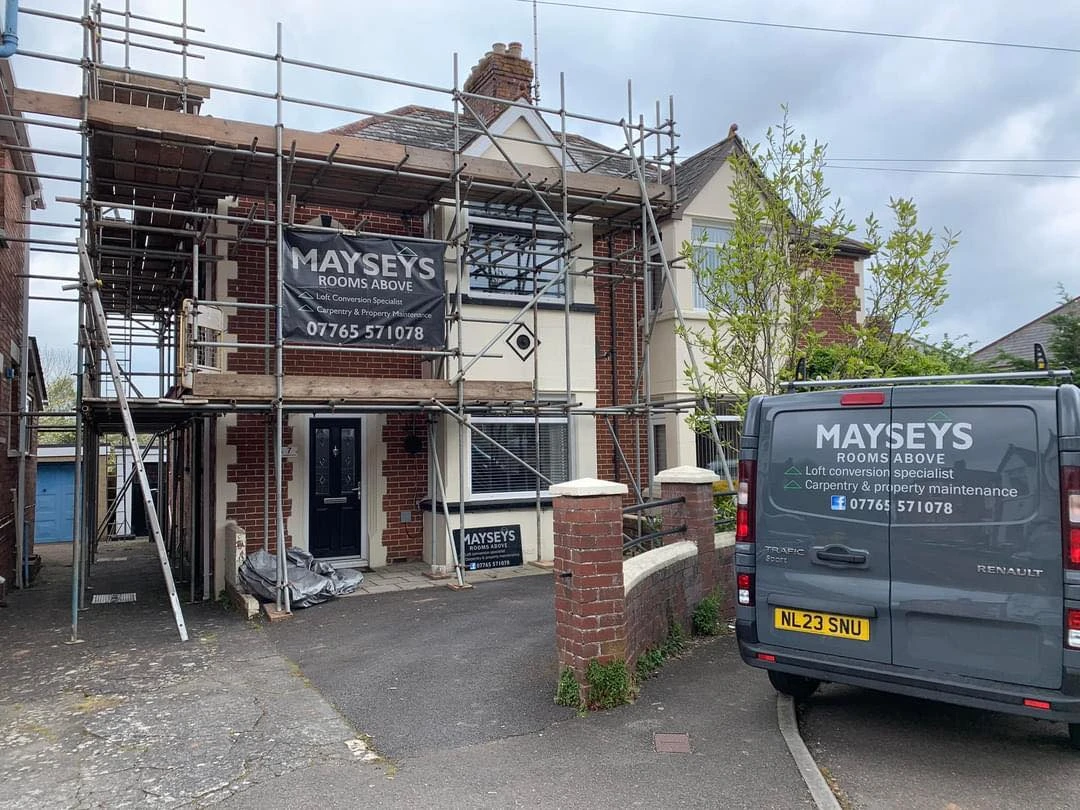 House under renovation with scaffolding, displaying a sign for Mayseys Rooms Above, alongside a gray Renault van.
