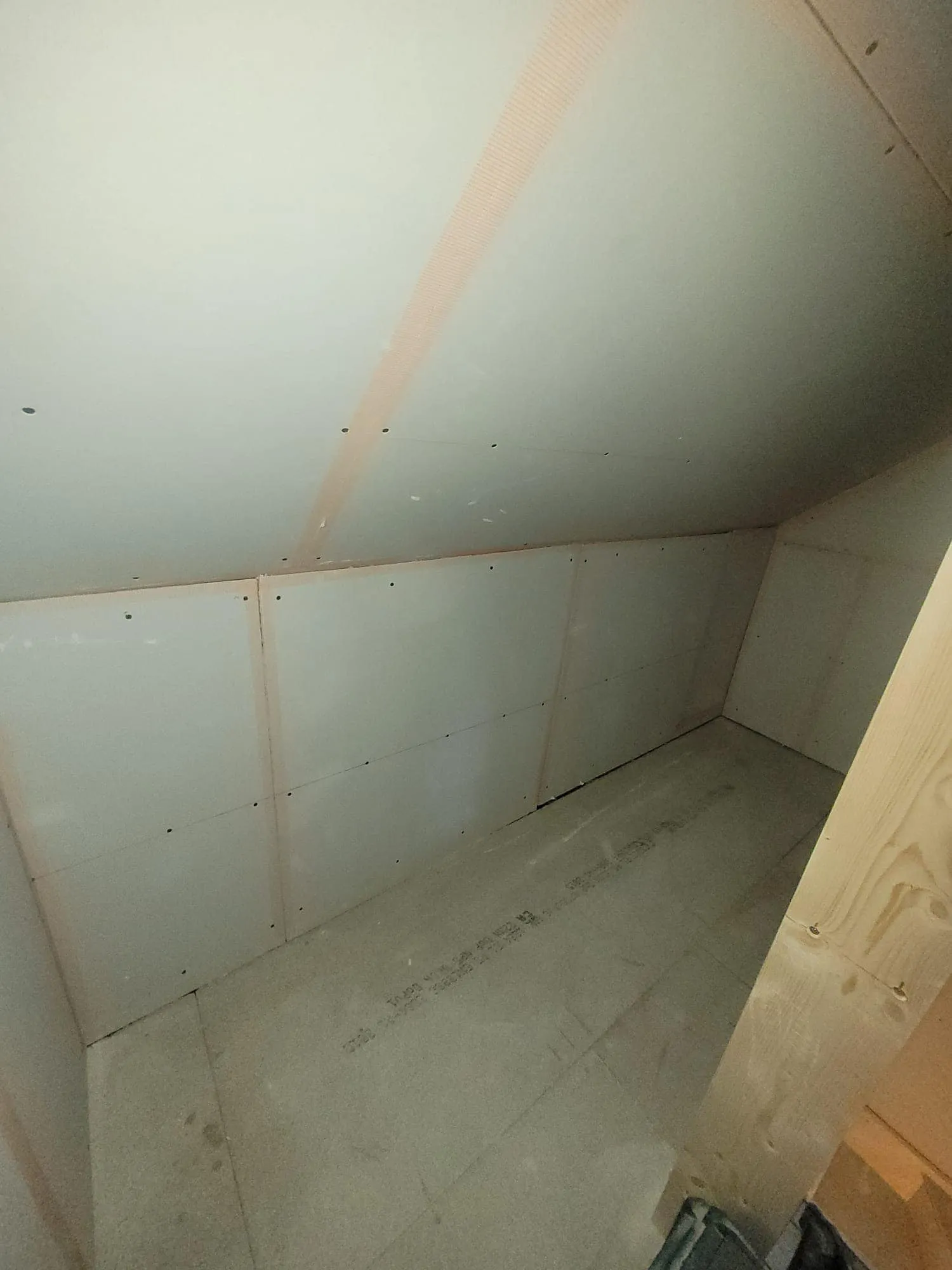 Interior view of an unfinished room with flat walls, a sloped ceiling, and bare flooring. The walls are partially panelled.