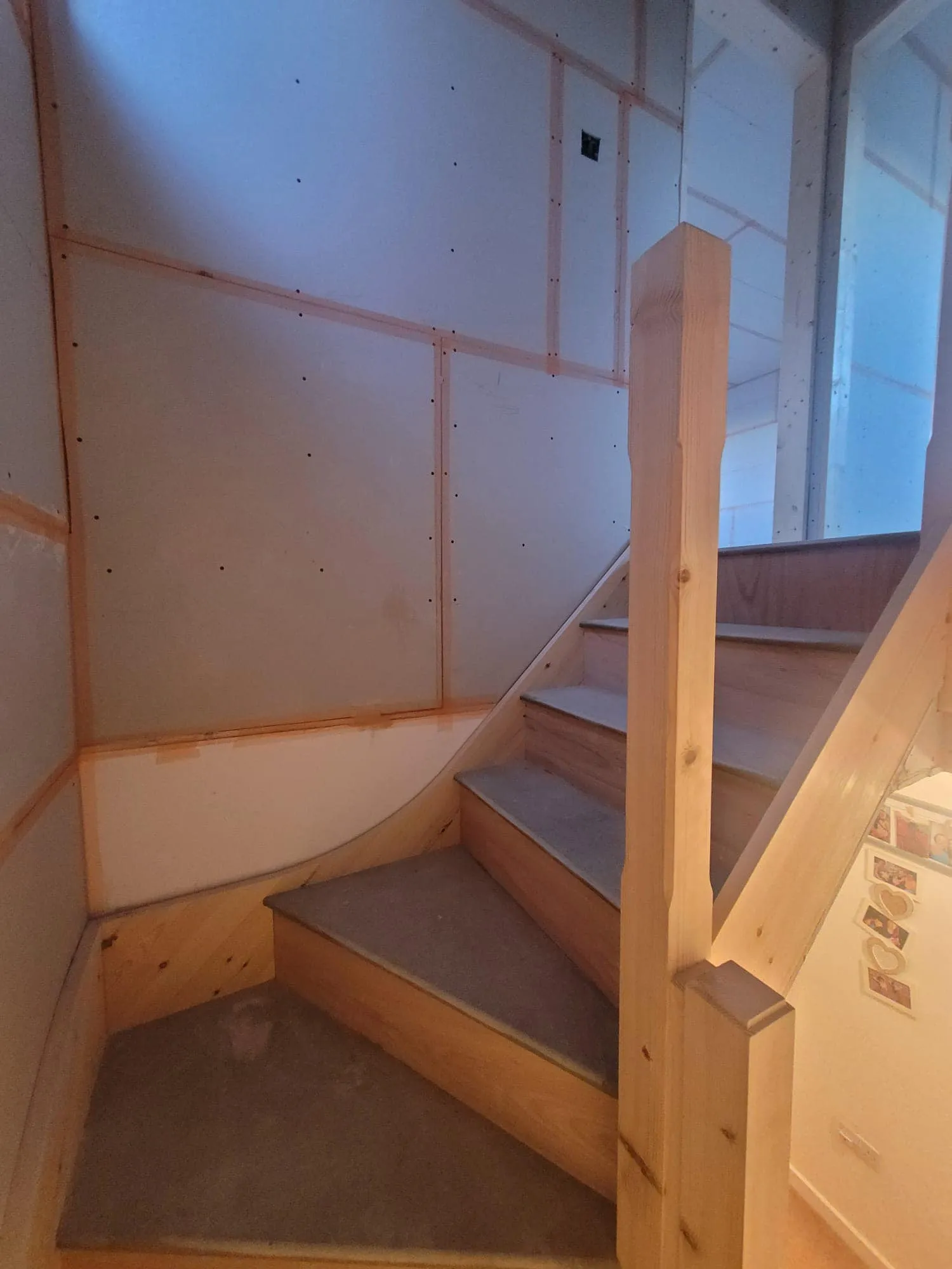 Staircase with wooden steps and railing, illuminated, adjacent to unfinished walls with insulation visible.