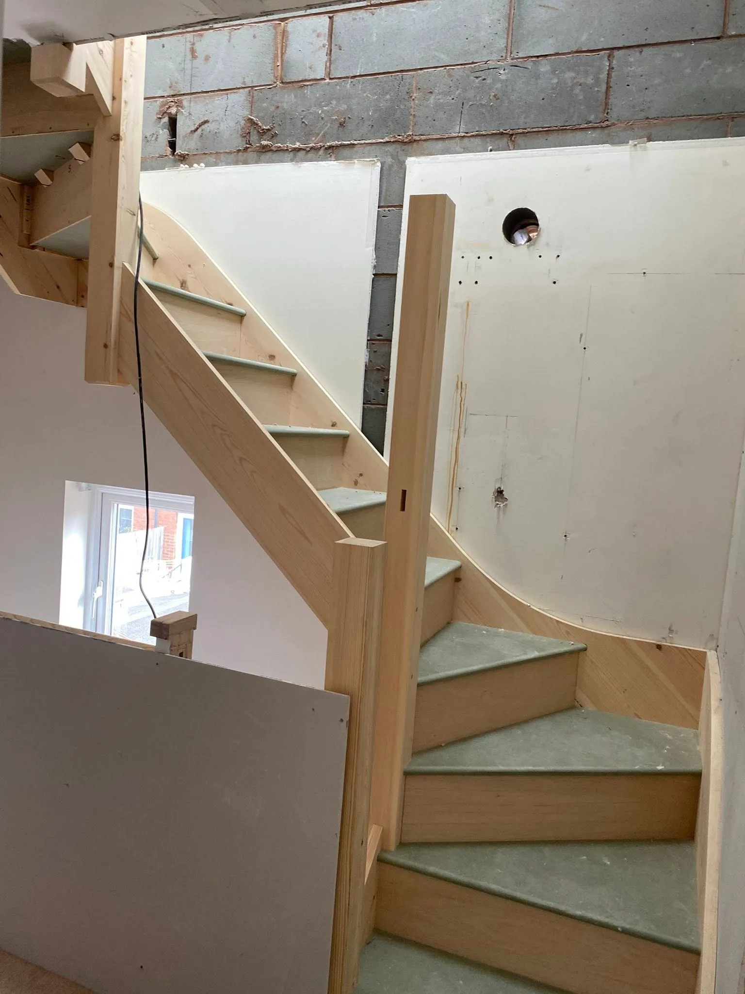 Wooden staircase during construction, featuring curved steps and unfinished walls in a residential setting.