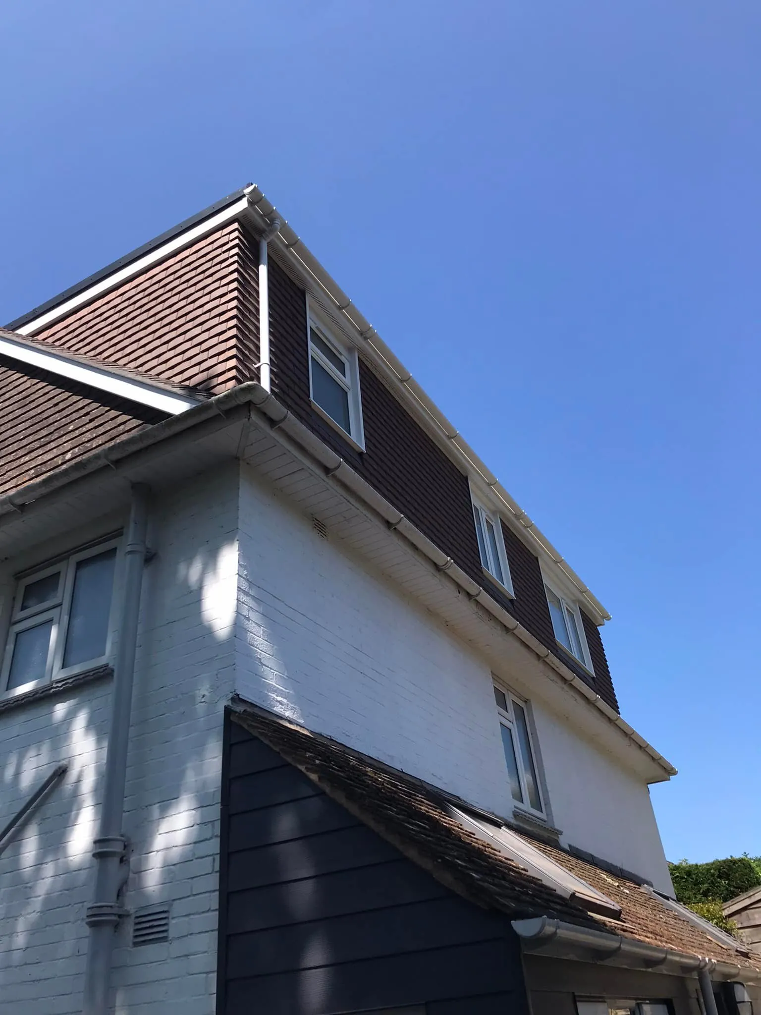 A house with a sloped roof, featuring brown shingles and white walls, set against a clear blue sky.
